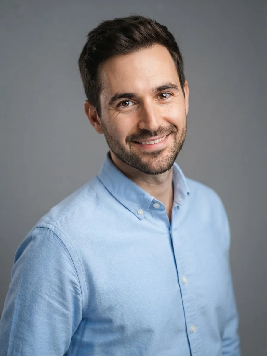 Man in a light blue shirt with his head tilted a few degrees toward his raised shoulder, warm smile
